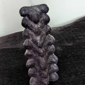 May include: A black and purple candle with a textured, rough surface. The candle is shaped like a stack of small, rounded blocks.