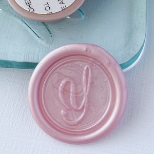 May include: A set of four adhesive labels with instructions to remove the liner to expose the adhesive. The labels are stacked on a light blue glass surface. A pink wax seal with a letter 'd' is in the foreground.