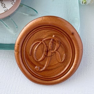 May include: A copper-colored wax seal with the initials "OR" in a cursive script. The seal is on a clear glass surface with a dragonfly design. There are three adhesive labels with instructions to remove the liner to expose the adhesive.