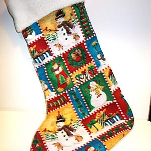 May include: A Christmas stocking with a white faux fur cuff. The body of the stocking is patterned with colorful squares featuring snowmen, wrapped gifts, and Christmas wreaths. The squares are outlined with a white dotted border.