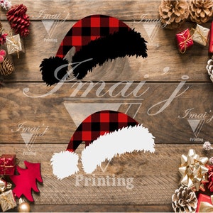 May include: Two red and black plaid Santa hats with white fur trim. The hats are on a wooden background with Christmas decorations.