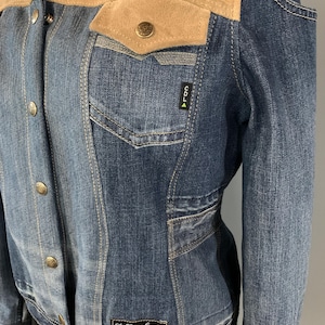 Peut inclure: Veste en jean bleue avec empiècement et rabats de poches en daim beige. Elle comporte des boutons, des poches avant et les inscriptions "COLD" et "Stella in dreams" sur la veste.