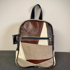 Peut inclure: Un sac à dos en cuir patchwork dans les tons marron, beige et blanc. Le sac est doté d'une poche avant zippée et d'une poignée noire. Le design comprend des formes géométriques et une étiquette de marque.