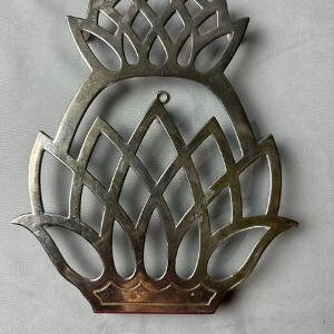 May include: Silver pineapple-shaped hot pad with a decorative, intricate design. The hot pad is made of metal and has a shiny finish.