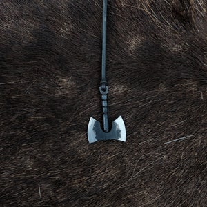 May include: A small black axe pendant with a leather cord hanging from a brown furry surface.
