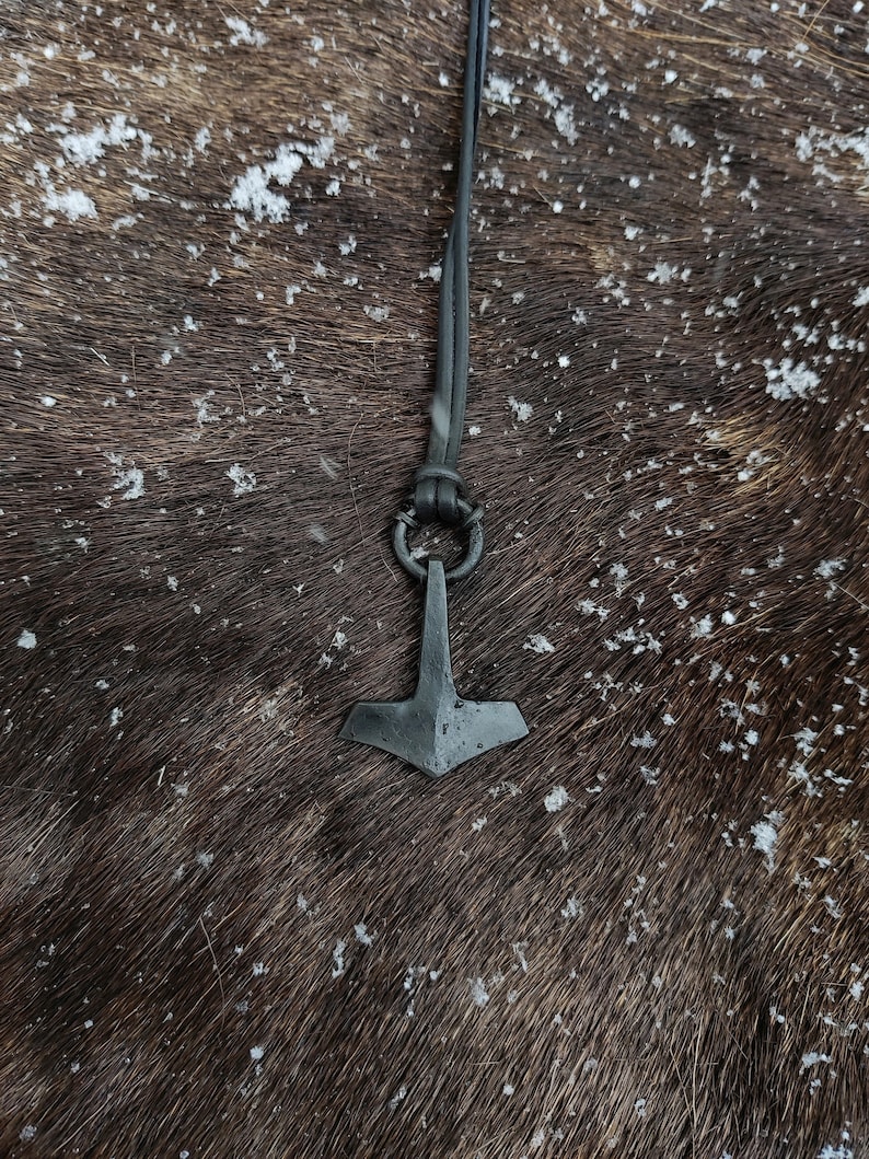 Pode incluir: Um colar de couro preto com um pingente de Mjolnir prateado. O pingente &eacute; uma r&eacute;plica do martelo de Thor da mitologia n&oacute;rdica.