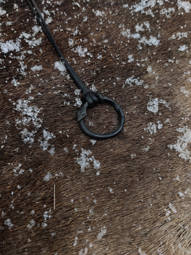 May include: A close-up of a black leather strap with a metal ring attached. The strap is lying on a brown surface with white specks.