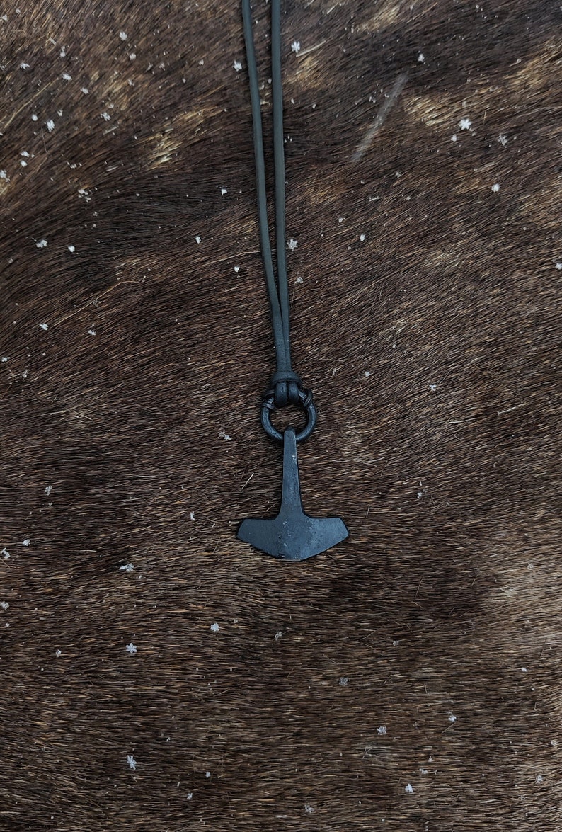 May include: A black metal Mjolnir pendant necklace with a black leather cord. The pendant is a replica of Thor's hammer.