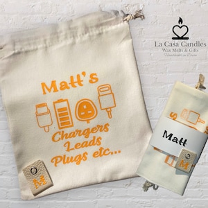 May include: Two white canvas bags with orange text and icons. The larger bag says "Matt's Chargers Leads Plugs etc..." and the smaller bag says "Matt". Both bags have a small white tag with the letter "M" on it.