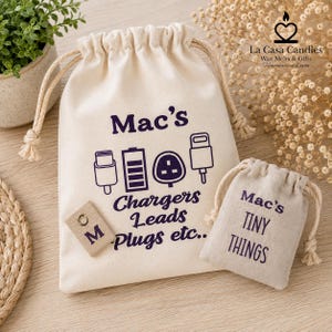 May include: Two off-white cotton drawstring bags with dark purple text and graphics. The larger bag features the text "Mac's Chargers Leads Plugs etc.." with icons of a USB-C connector, battery, UK plug, and cable. The smaller bag reads "Mac's TINY THINGS".