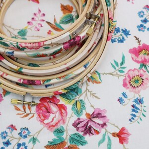May include: A set of wooden embroidery hoops with a floral pattern. The hoops are stacked on top of each other and have a white background with pink, blue, and green flowers.