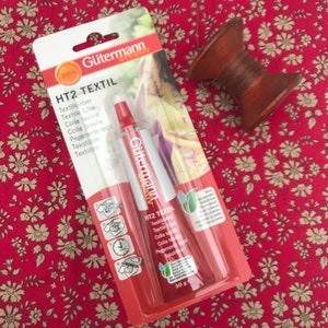 Peut inclure: Un tube rouge de colle textile Gütermann HT2 Textil avec des instructions sur l'emballage. Le tube est de 30 grammes et est étiqueté en allemand et en anglais.