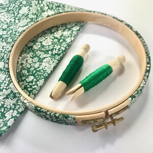 May include: A wooden embroidery hoop with a green floral fabric stretched over it. Two spools of green embroidery floss are included.