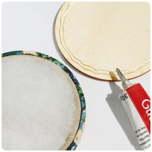 May include: A round wooden base with a white glue border, a tube of glue, and a round fabric base with a white cotton centre and a floral pattern border.