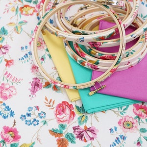 May include: A set of embroidery hoops with floral patterns on a white background with floral designs. The hoops are stacked on top of each other and are surrounded by fabric.