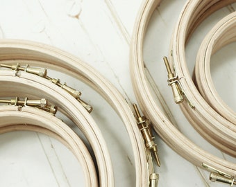 May include: A set of four wooden embroidery hoops with brass tightening screws. The hoops are nested together, with the largest hoop at the bottom and the smallest hoop at the top.