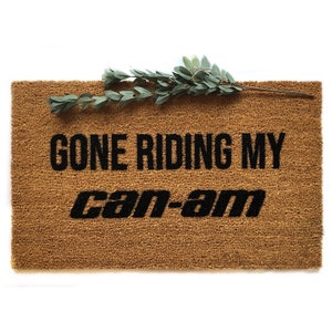 May include: A brown coir doormat with the text "Gone Riding My Can-Am" in black lettering.