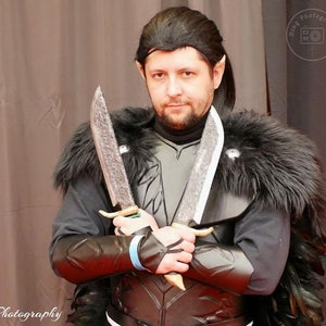 May include: A person dressed as a fantasy character, wearing a black costume with a fur collar and holding two silver daggers.