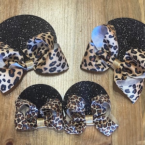 May include: Three leopard print hair bows with gold centers on black glitter circles.