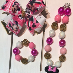 May include: A pink, white, and gold beaded necklace and bracelet set with a Minnie Mouse charm. The beads are iridescent and some have a sparkly finish.
