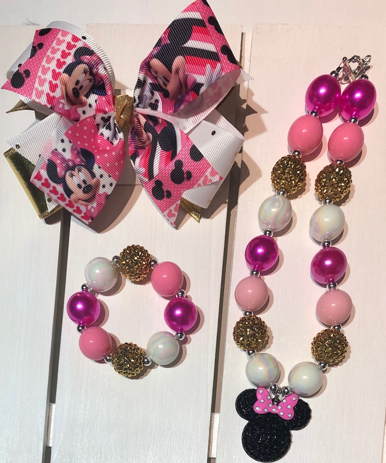 May include: A pink, white, and gold beaded necklace and bracelet set with a Minnie Mouse charm. The beads are iridescent and some have a sparkly finish.