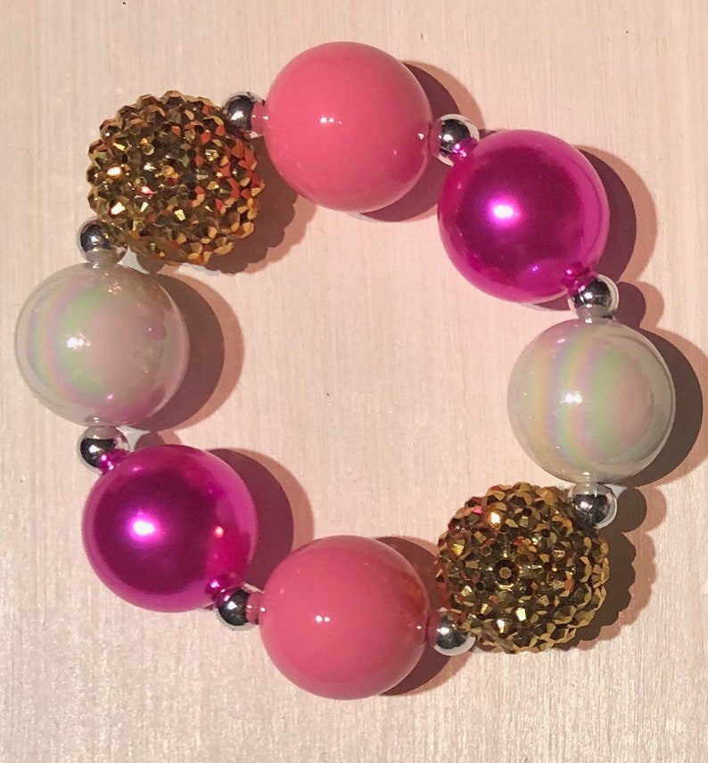 May include: A pink and gold beaded bracelet with iridescent white beads and silver spacers.
