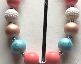 May include: A pink, blue and white beaded necklace with a Moana charm. The charm is a cartoon image of Moana holding a spear.