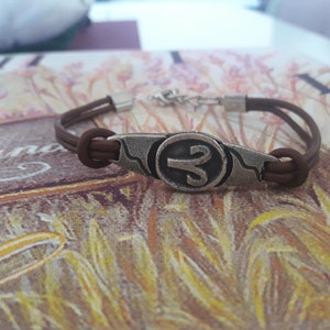May include: A brown leather bracelet with a silver charm featuring the astrological symbol for Aries.