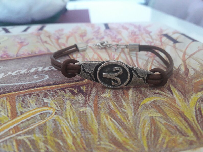 May include: A brown leather bracelet with a silver charm featuring the astrological symbol for Aries.