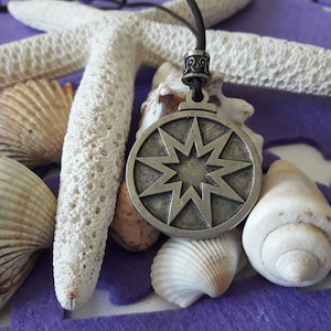 May include: A silver pendant featuring an eight-pointed star design, suspended from a black cord. The pendant is surrounded by seashells on a purple background.