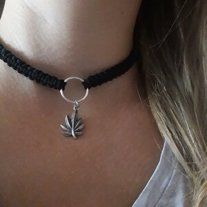 May include: A black choker necklace with a silver marijuana leaf pendant.
