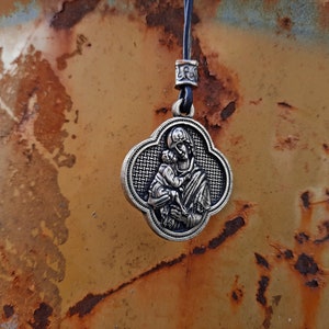 May include: A silver pendant necklace with a religious image of a mother and child. The pendant is in the shape of a four-leaf clover and has a woven pattern.