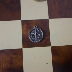 May include: A silver pendant with a Christian symbol, the Chi Rho, surrounded by a circle of small beads. The symbol is a combination of the first two letters of the Greek word for Christ, '&Chi;&Rho;&Iota;&Sigma;&Tau;&Omicron;&Sigma;'.
