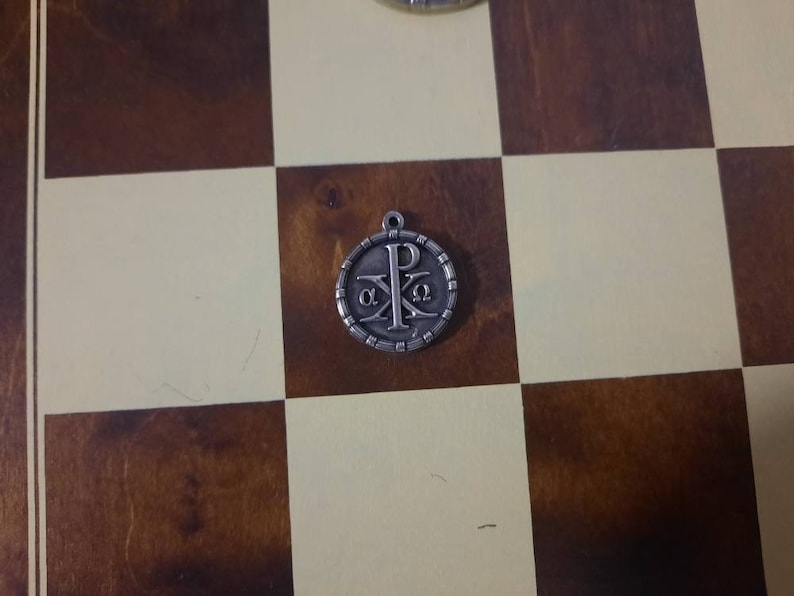 May include: A silver pendant with a Christian symbol, the Chi Rho, surrounded by a circle of small beads. The symbol is a combination of the first two letters of the Greek word for Christ, '&Chi;&Rho;&Iota;&Sigma;&Tau;&Omicron;&Sigma;'.