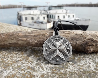 May include: A silver pendant necklace with a star-shaped design. The pendant is round and has a textured surface. The necklace is on a black leather cord.