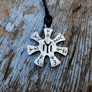 May include: A silver-toned pendant necklace with a star-shaped design. The pendant features a symbol in the centre and runes around the edges. The necklace is on a black cord.