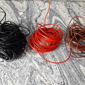 May include: Three spools of leather cord in black, red, and brown. The cords are coiled and ready for crafting projects.