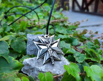 May include: A silver-toned pendant necklace with a star-shaped design featuring a figure of a person with outstretched arms. The pendant is hanging from a black leather cord and is resting on a gray rock.