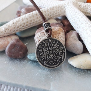 May include: A silver pendant necklace with a brown leather cord. The pendant features a five-pointed star with the words "1 2 3 TRA 6 GRAM 4 5 1 2 3 TRA 6 GRAM 4 5" around the perimeter.