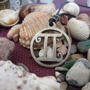 May include: A silver necklace with a circular pendant featuring the Gemini zodiac symbol. The pendant is surrounded by various seashells and stones.