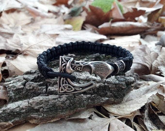 May include: A black paracord bracelet with a silver axe charm. The axe charm has intricate details and a knot design.