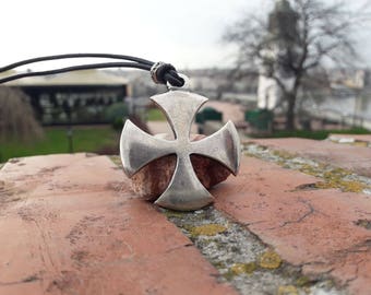 May include: A silver cross pendant with a leather cord. The cross is a four-pointed design with a slightly raised center.