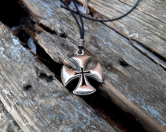 May include: A silver cross pendant with a black cord necklace. The cross has a simple design with a raised center and four points.