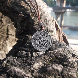 May include: A silver pendant necklace with a five-pointed star and the words "1 2 3 4 5 6 7 8 9 10 11 12" around the star. The pendant is hanging from a brown leather cord.