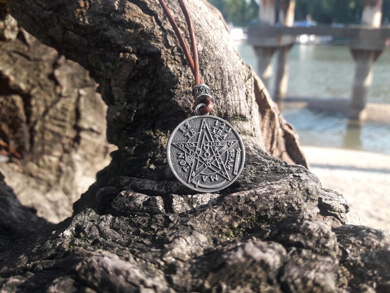 May include: A silver pendant necklace with a five-pointed star and the words "1 2 3 4 5 6 7 8 9 10 11 12" around the star. The pendant is hanging from a brown leather cord.