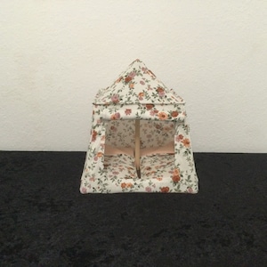 Op de afbeelding: Een witte tent met bloemenprint en een houten frame. De tent heeft twee bedden binnenin.