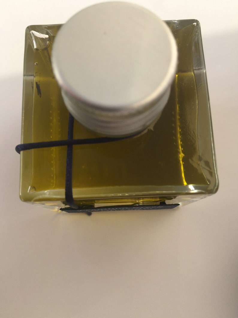 Pode incluir: Uma garrafa de vidro transparente com uma tampa prateada e um cord&atilde;o preto amarrado ao redor do pesco&ccedil;o. A garrafa est&aacute; cheia de um l&iacute;quido dourado.