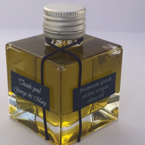 Pode incluir: Uma pequena garrafa de vidro de azeite extra virgem grego premium com uma tampa prateada e uma fita preta amarrada ao redor do pesco&ccedil;o. A garrafa tem um r&oacute;tulo que diz "Azeite extra virgem grego premium" e uma nota de agradecimento que diz "Obrigado! George & Mary".