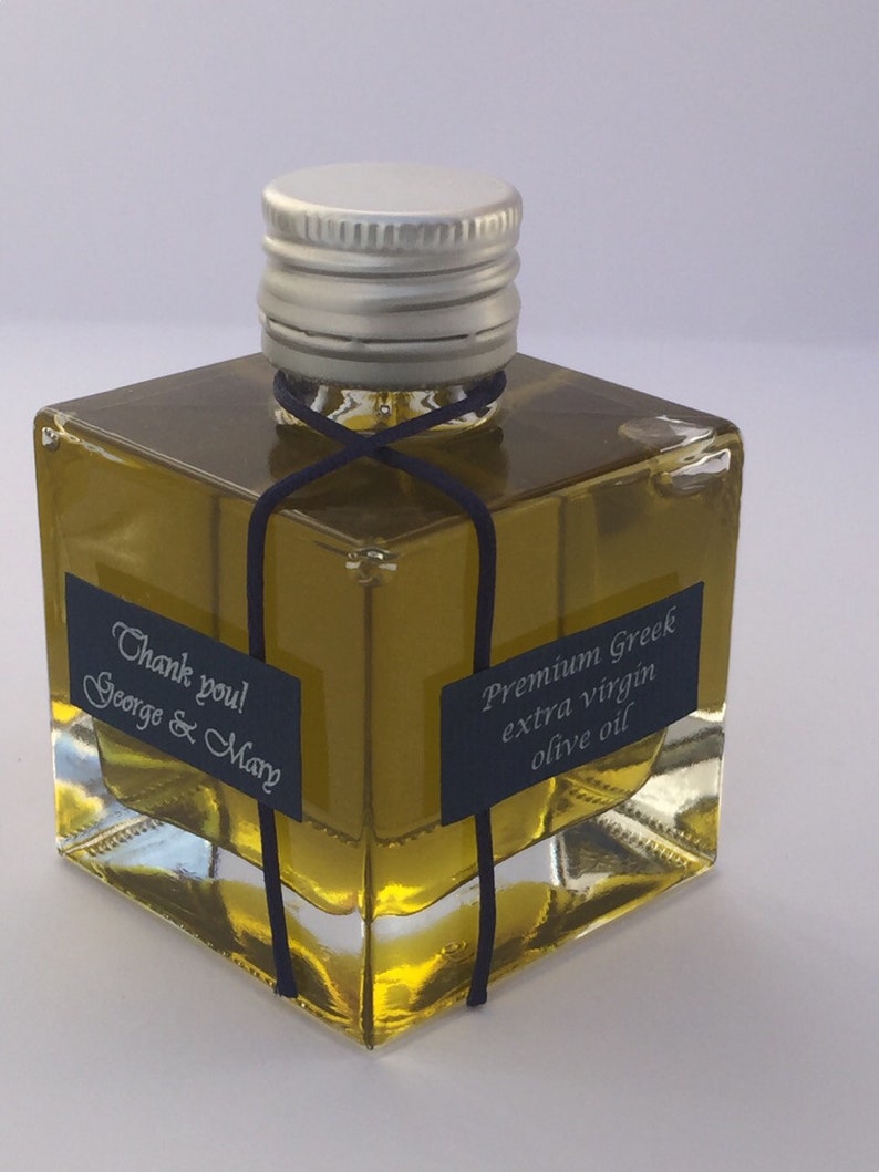 Pode incluir: Uma pequena garrafa de vidro de azeite extra virgem grego premium com uma tampa prateada e uma fita preta amarrada ao redor do pesco&ccedil;o. A garrafa tem um r&oacute;tulo que diz "Azeite extra virgem grego premium" e uma nota de agradecimento que diz "Obrigado! George & Mary".