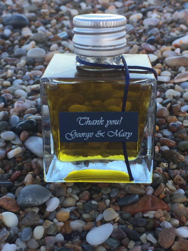 Pode incluir: Uma pequena garrafa de vidro transparente cheia de um l&iacute;quido dourado. A garrafa tem uma tampa prateada e uma fita preta amarrada ao redor do pesco&ccedil;o. Um r&oacute;tulo preto na garrafa diz "Obrigado! George & Mary".
